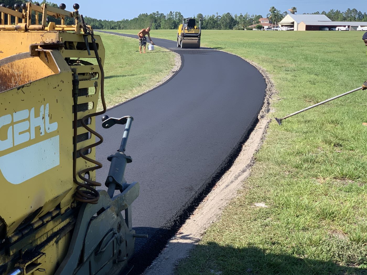 Paver and roller laying new asphalt on a curved driveway