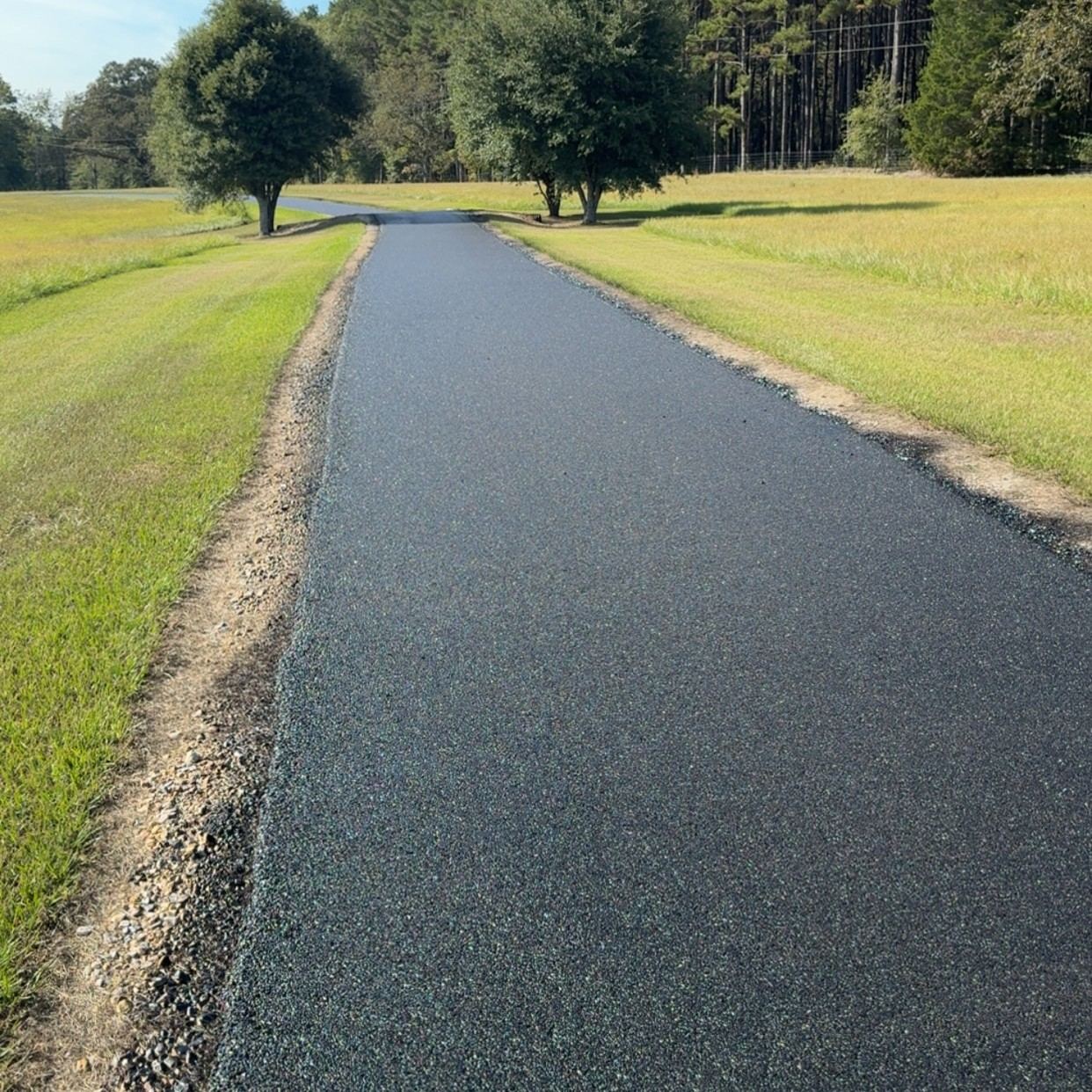 Freshly sealcoated driveway between green fields
